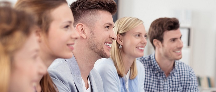 5 Menschen sitzen und lächeln, sie nehmen an eine Schulung teil.