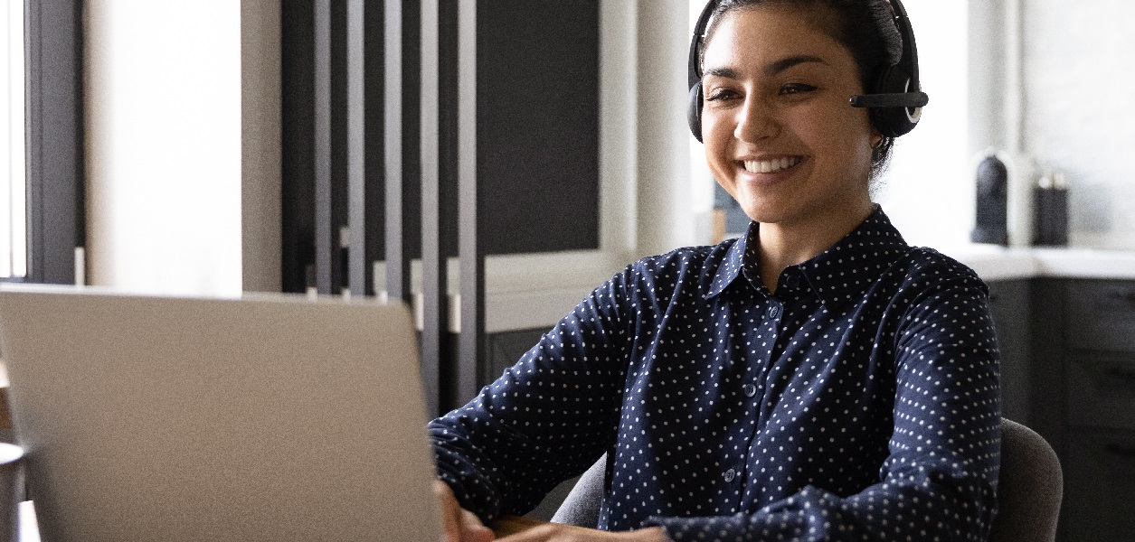 Eine Frau sitzt am Laptop und hat einen Headset. Sie leitet einen Workshop.